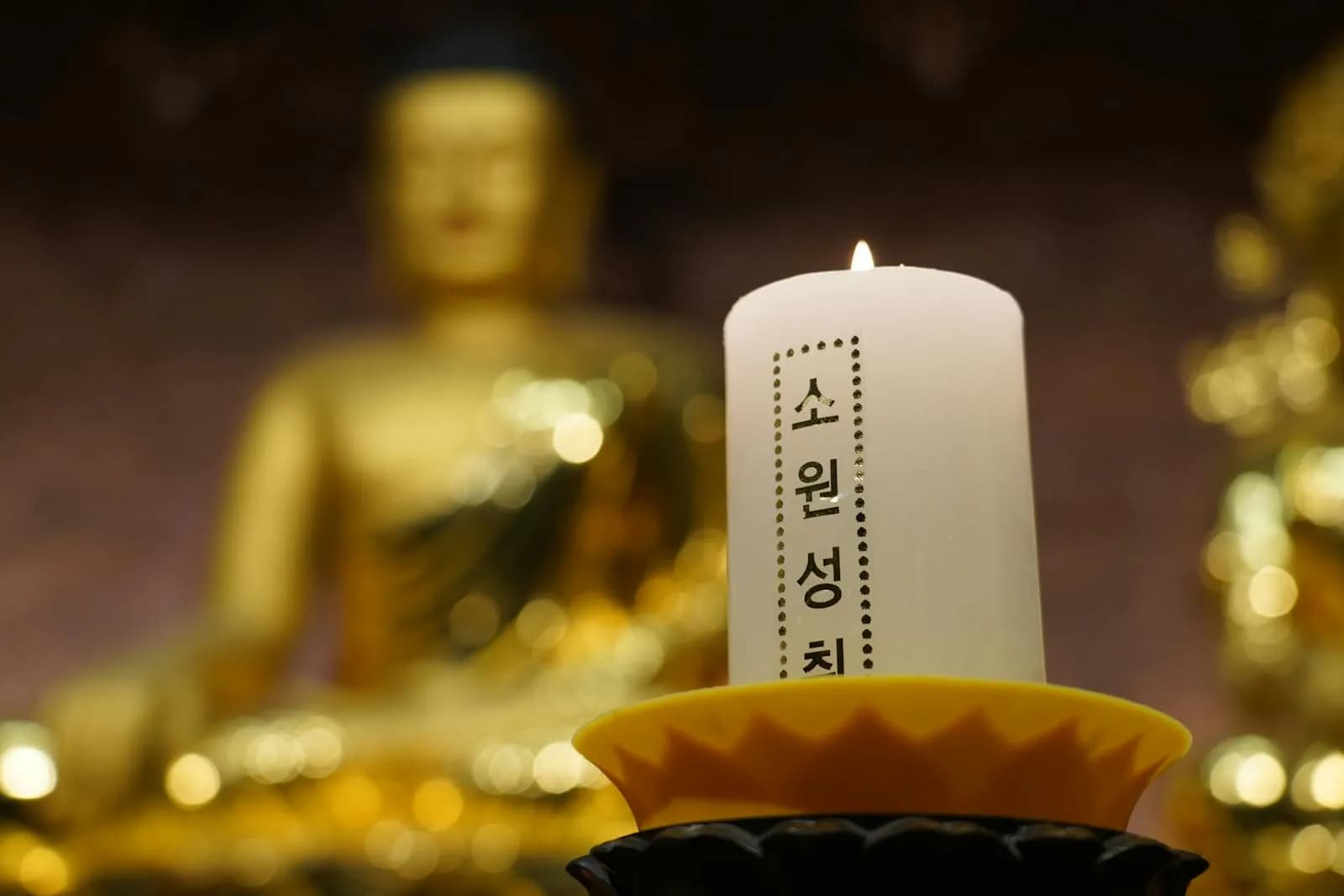 A single candle glowing in front of a golden Buddha statue inside a Seoul temple