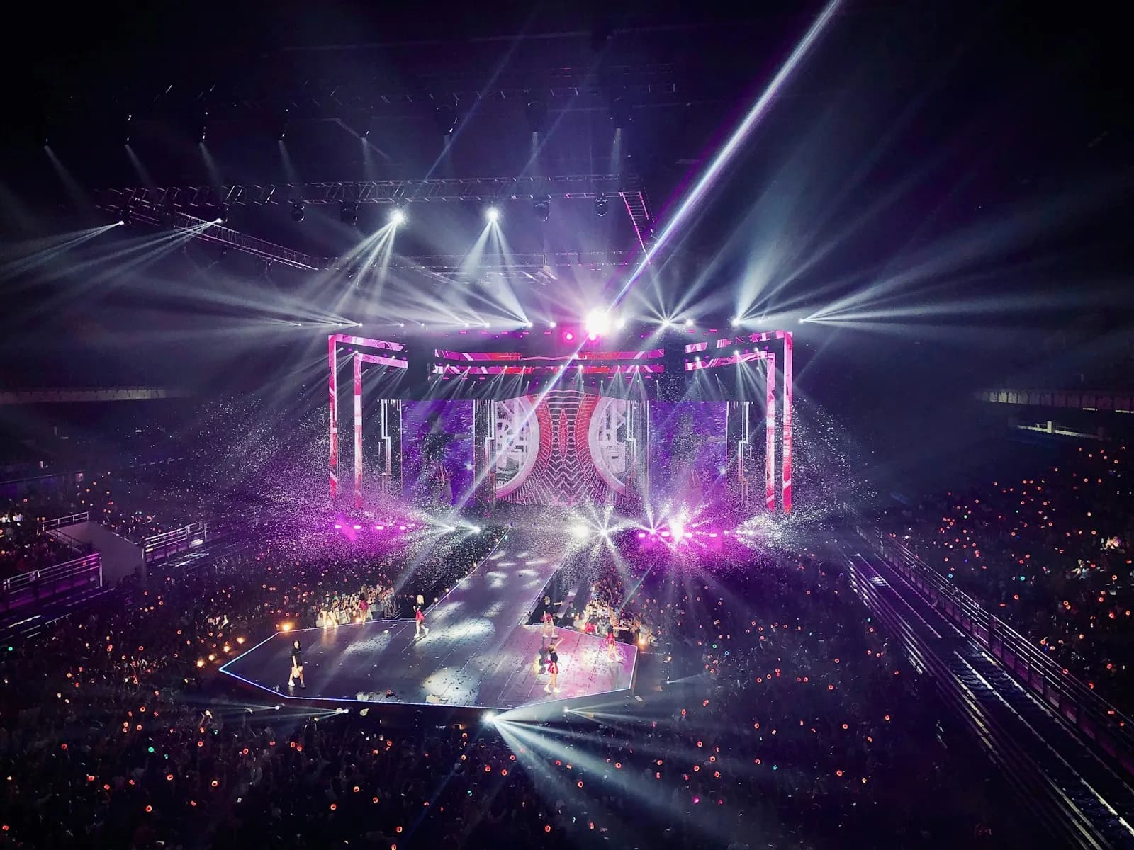 K-pop performer on stage with audience lightsticks glowing in front
