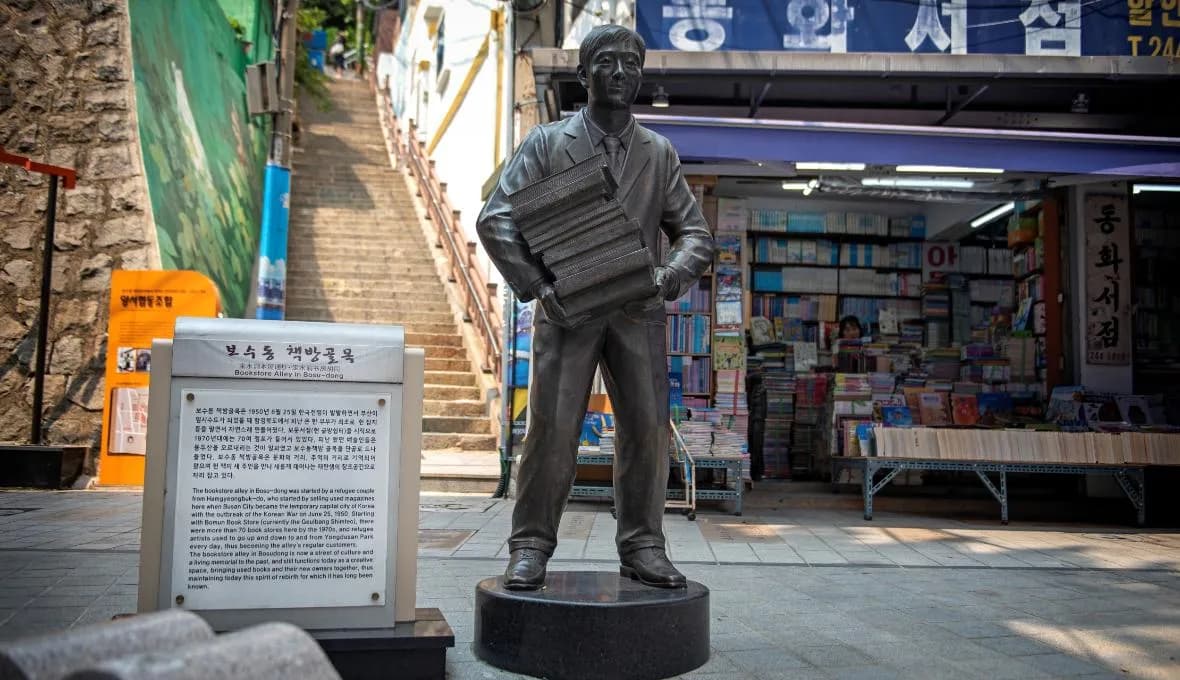 Bronze statue of a book seller carrying books at the Bosu-dong Book Street stairway with information plaque
