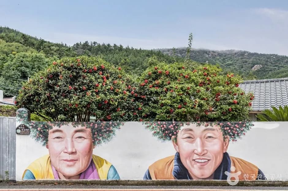 The camellia-perm mural of an elderly couple, with red camellia trees forming their hair, at the Gidong intersection on Amtae-do, Sinan