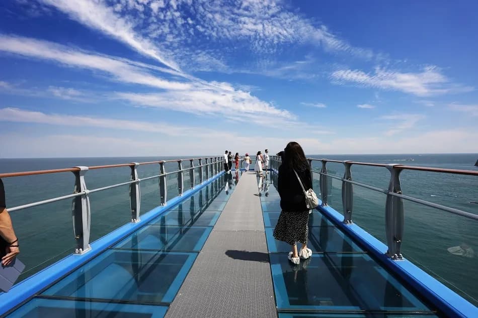 Visitors on the Oryukdo Skywalk glass observation deck extending over the sea in Busan, where BTS Jimin's 2015 vlog photo was taken