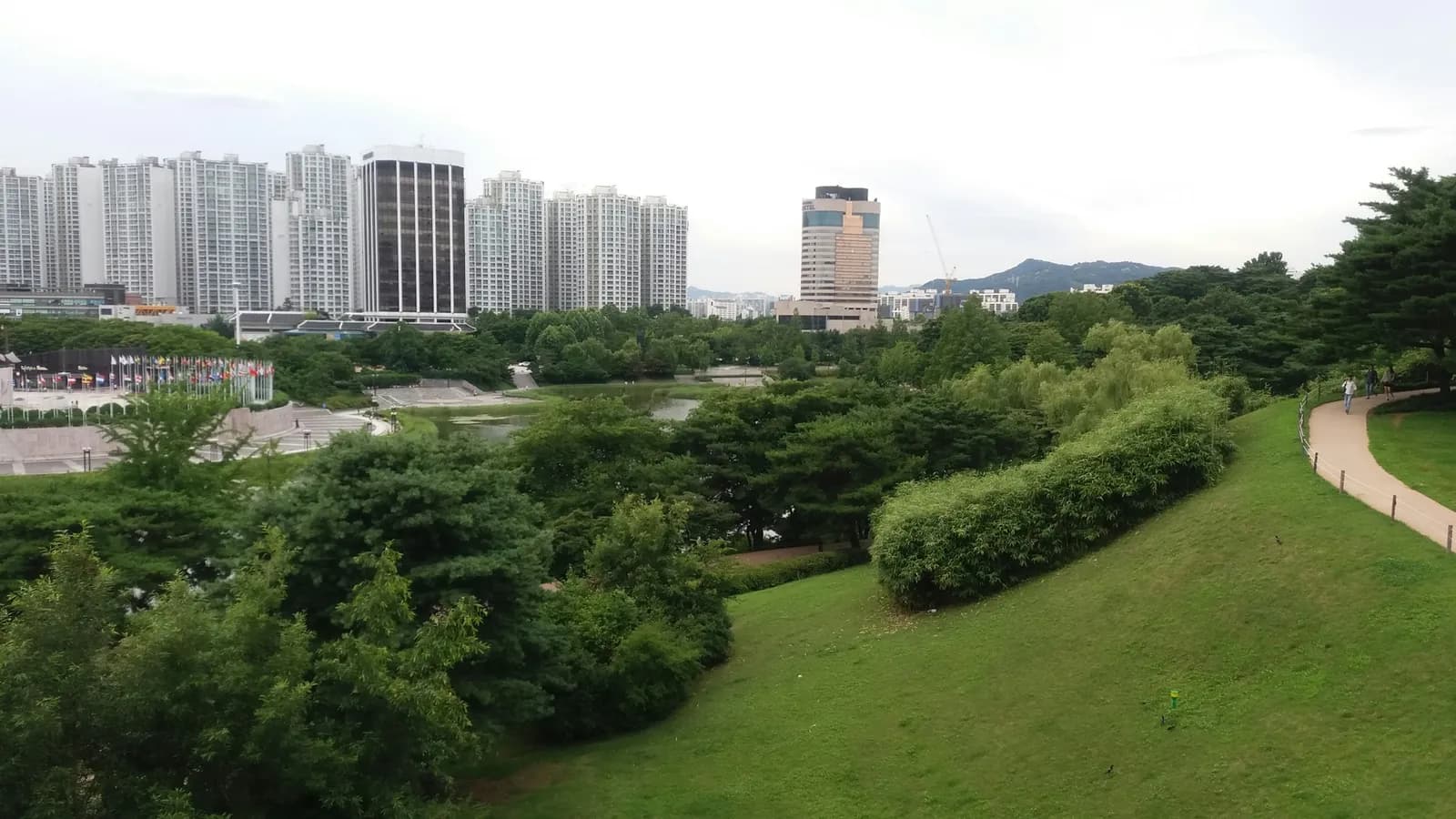 Tree-lined walking path in a Seoul neighborhood park with buildings in the background