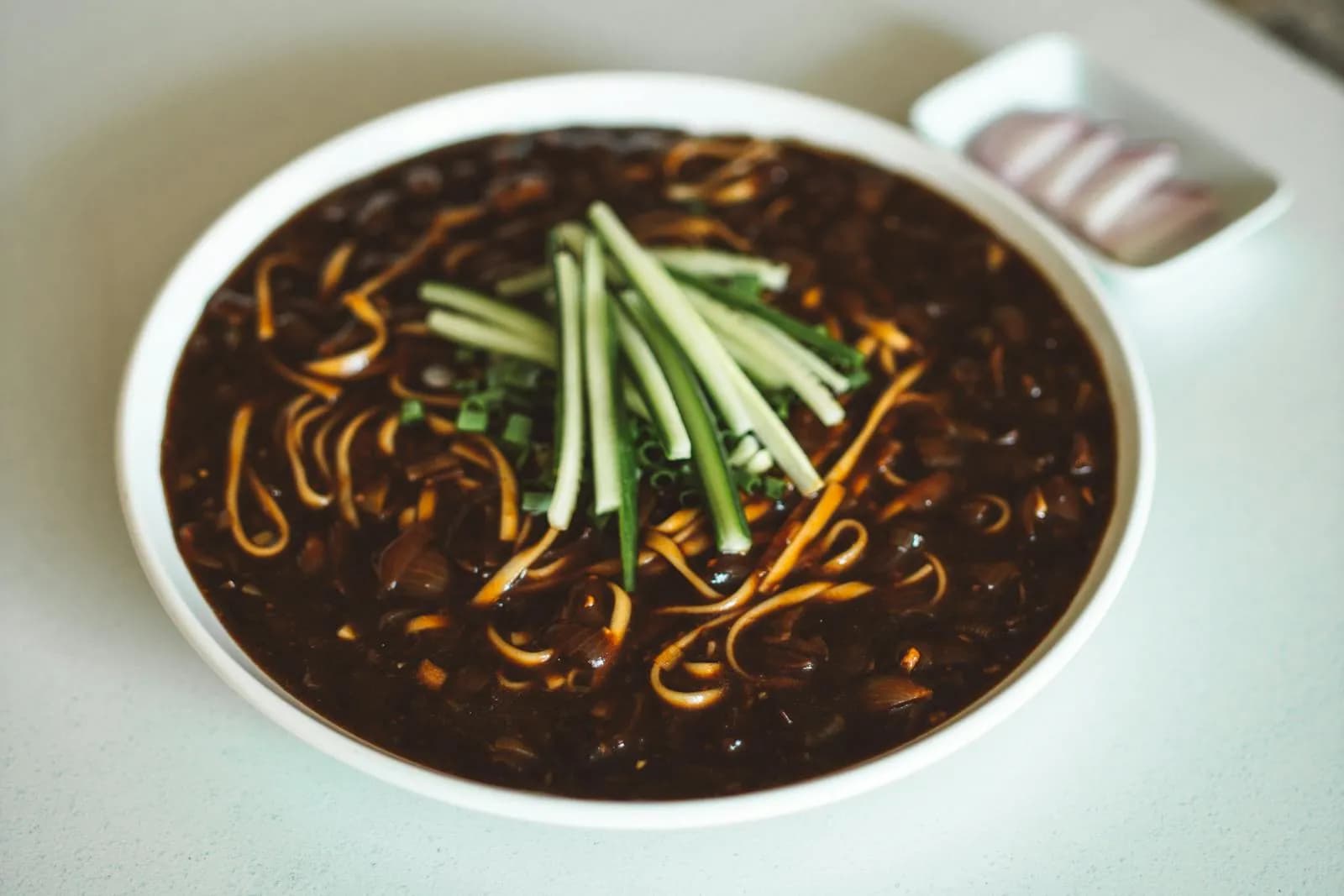 Bowl of jajangmyeon with black bean sauce and fresh cucumber garnish