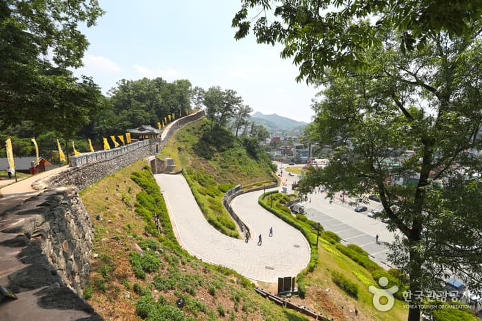 Stone fortress walls and a paved path winding over the green ridges of Gongsanseong